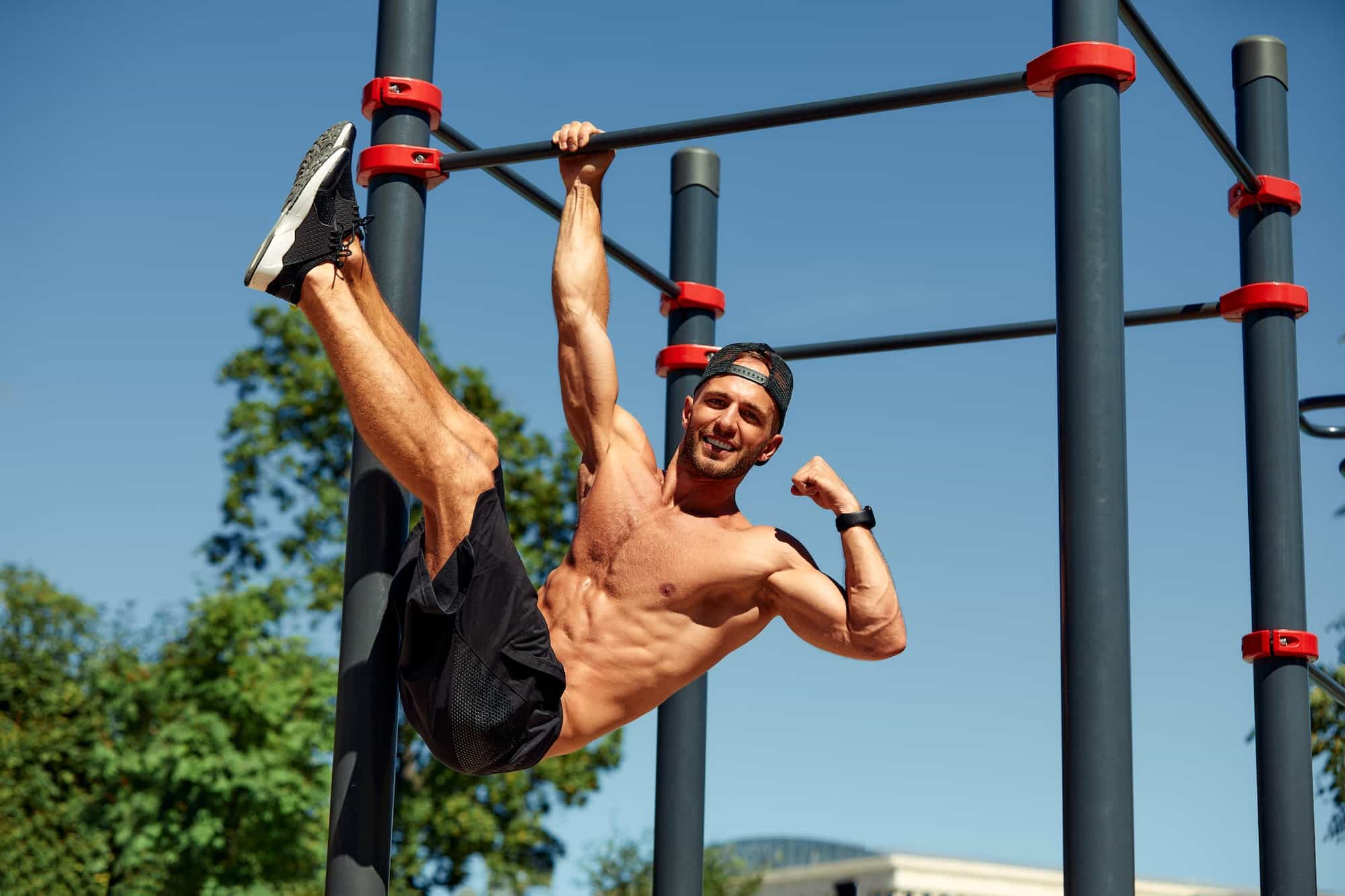 Athletic young man hanging from the bars at the calisthenics gym outdoors smiling